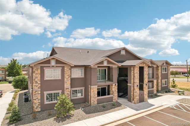 view of front facade featuring stone siding, a shingled roof, uncovered parking, and stucco siding