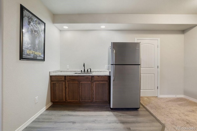 kitchen featuring stainless steel refrigerator, dark brown cabinetry, sink, and light colored carpet