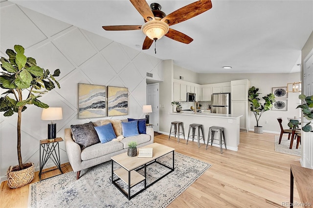 living room featuring light wood-type flooring, ceiling fan, and baseboards