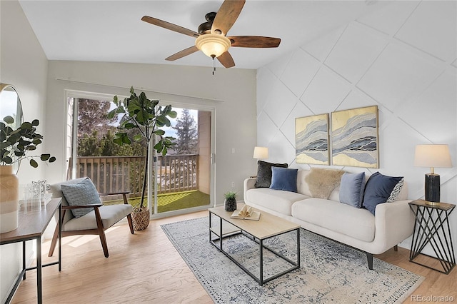 living area with lofted ceiling, an accent wall, light wood finished floors, and ceiling fan