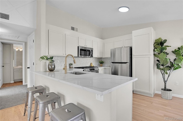 kitchen featuring stainless steel appliances, visible vents, a sink, a peninsula, and a kitchen breakfast bar