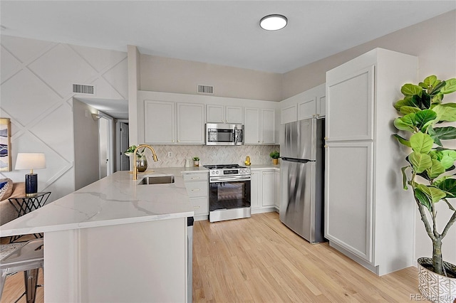 kitchen with a breakfast bar area, light stone counters, a peninsula, stainless steel appliances, and a sink