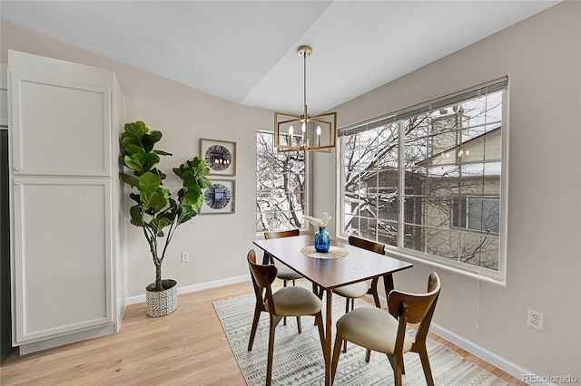 dining area with baseboards, vaulted ceiling, light wood finished floors, and an inviting chandelier