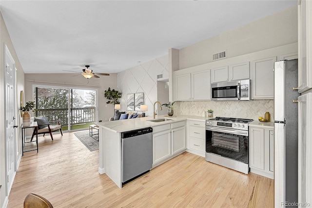 kitchen with stainless steel appliances, light countertops, light wood-style flooring, a sink, and a peninsula