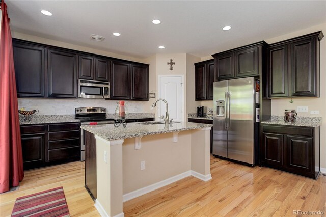12513 Grape St, Thornton, CO 80241 - kitchen featuring stainless steel appliances, light wood-style floors, a kitchen island with sink, a kitchen breakfast bar, and light stone countertops