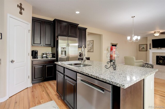 12513 Grape St, Thornton, CO 80241 - kitchen featuring appliances with stainless steel finishes, open floor plan, light wood-style floors, an island with sink, and a tiled fireplace
