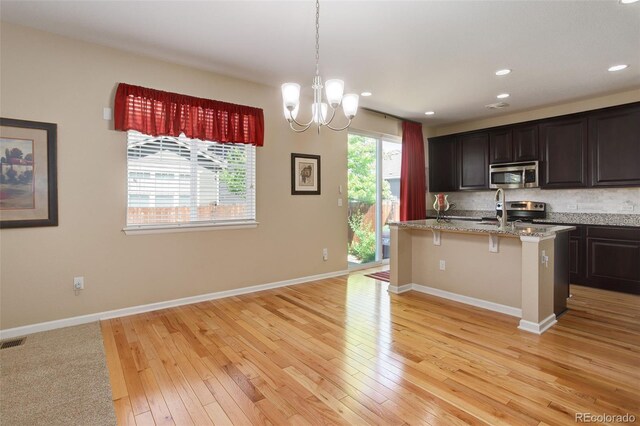 12513 Grape St, Thornton, CO 80241 - kitchen featuring appliances with stainless steel finishes, backsplash, light wood-style floors, a breakfast bar, and a kitchen island with sink