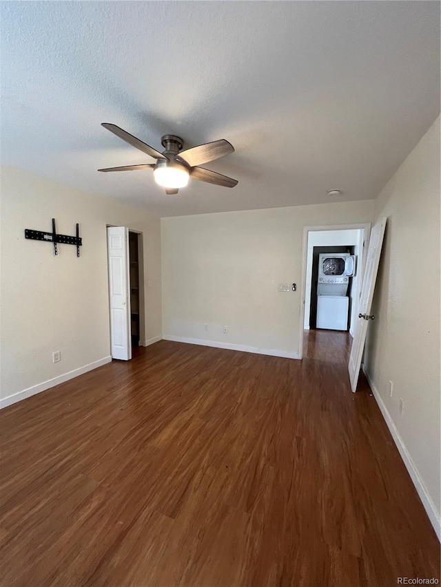 spare room with ceiling fan, dark hardwood / wood-style flooring, stacked washer / dryer, and a textured ceiling