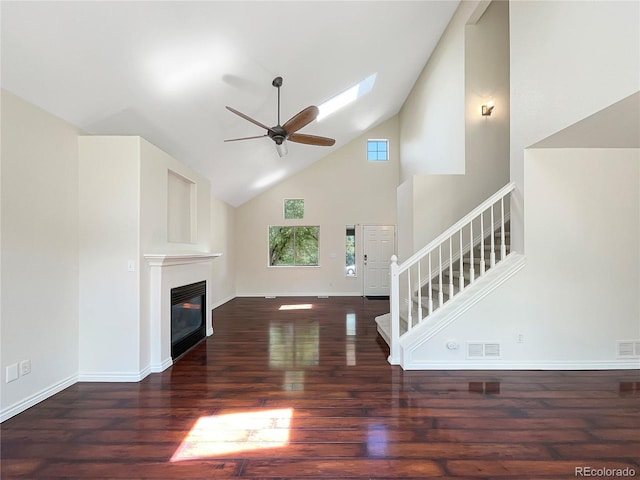 unfurnished living room with ceiling fan, a towering ceiling, dark wood-type flooring, and a skylight