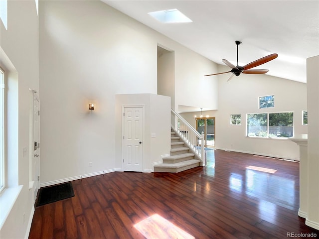 unfurnished living room with a skylight, high vaulted ceiling, dark wood-type flooring, and ceiling fan with notable chandelier