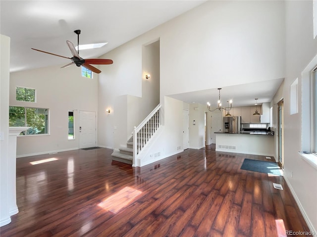 unfurnished living room with dark hardwood / wood-style flooring, high vaulted ceiling, and ceiling fan with notable chandelier