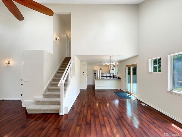 stairway featuring a wealth of natural light, a towering ceiling, ceiling fan with notable chandelier, and hardwood / wood-style flooring