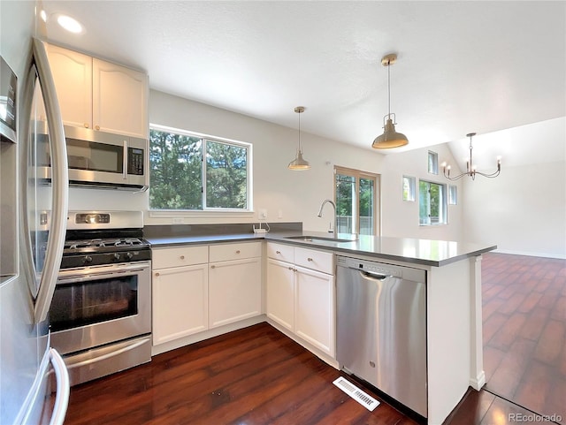 kitchen with sink, kitchen peninsula, pendant lighting, white cabinets, and appliances with stainless steel finishes