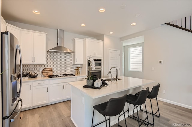 6581 E 148th Dr, Thornton, CO 80602 - kitchen featuring stainless steel appliances, wall chimney exhaust hood, light wood-style flooring, white cabinetry, and recessed lighting