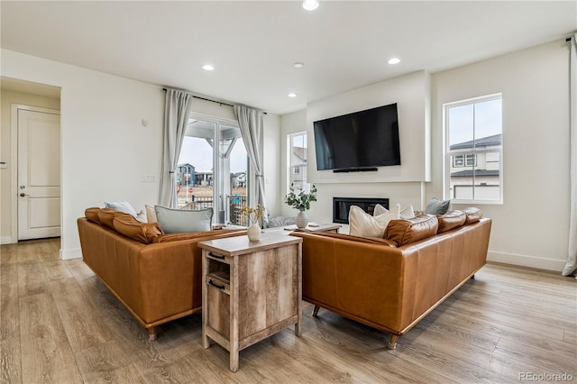 living room featuring baseboards, a glass covered fireplace, recessed lighting, and light wood-type flooring