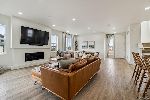 living area featuring stairway, recessed lighting, baseboards, a glass covered fireplace, and wood finished floors