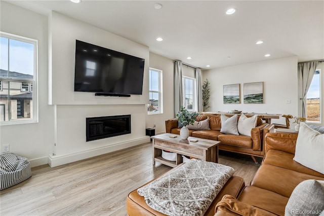 living area with a wealth of natural light, a glass covered fireplace, recessed lighting, and light wood-type flooring
