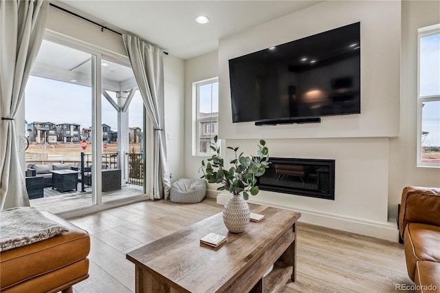 living area featuring baseboards, recessed lighting, wood finished floors, and a glass covered fireplace