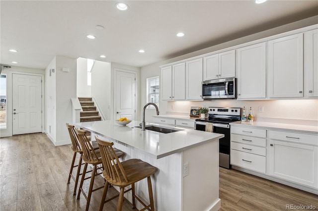 kitchen with a kitchen island with sink, a sink, light wood-style flooring, and appliances with stainless steel finishes