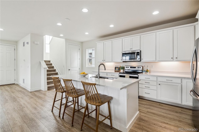 kitchen with a kitchen island with sink, a sink, stainless steel appliances, and light wood-type flooring