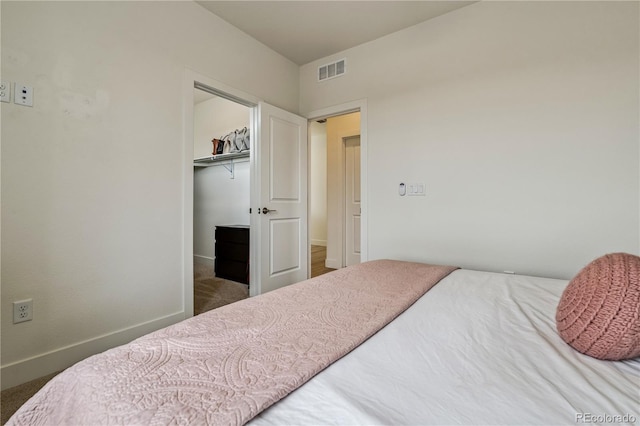 carpeted bedroom featuring a closet, a walk in closet, baseboards, and visible vents