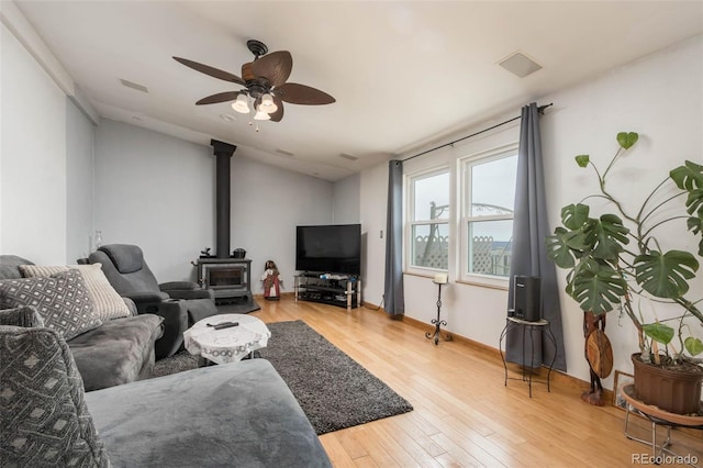 living room featuring ceiling fan, light wood-type flooring, vaulted ceiling, and a wood stove