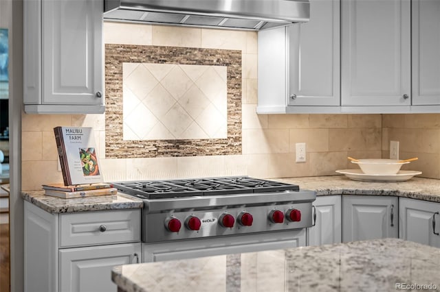 kitchen featuring decorative backsplash, light stone countertops, wall chimney range hood, white cabinetry, and stainless steel gas stovetop
