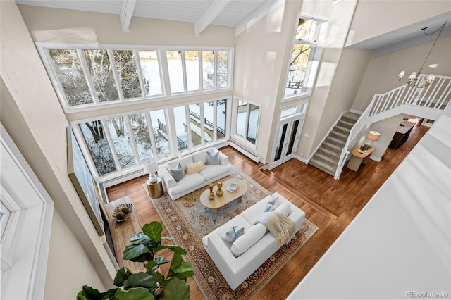 living room with a towering ceiling, wood finished floors, beamed ceiling, a notable chandelier, and stairs