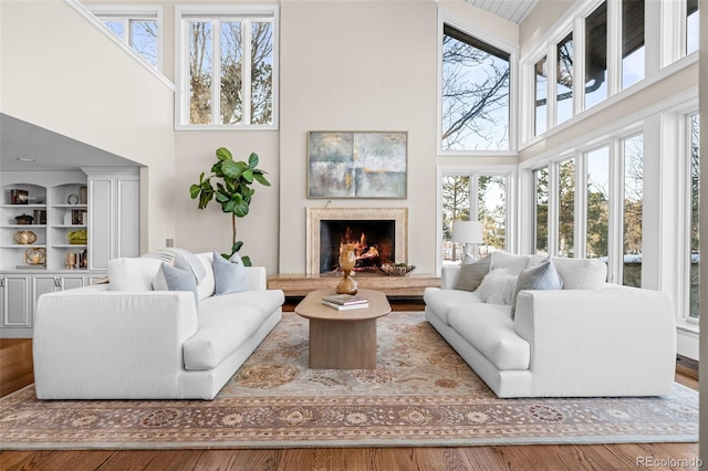 living room featuring wood finished floors, a premium fireplace, a healthy amount of sunlight, and a towering ceiling