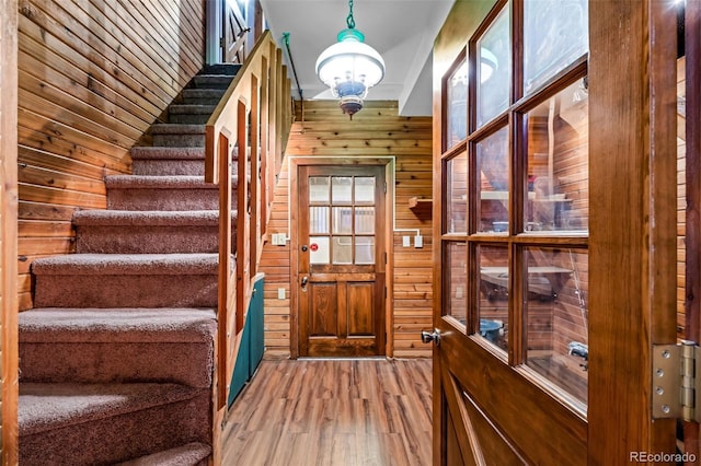 doorway to outside with wood finished floors, wooden walls, and stairway
