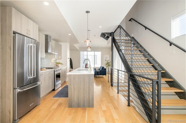 kitchen with wall chimney exhaust hood, high end appliances, modern cabinets, and light wood-type flooring