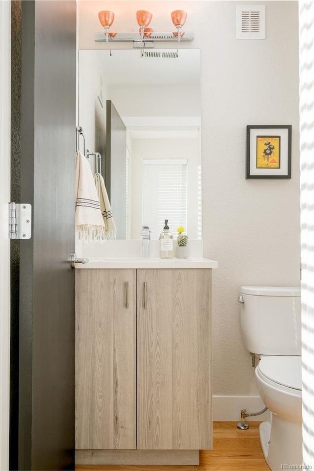 half bath with visible vents, baseboards, toilet, wood finished floors, and vanity