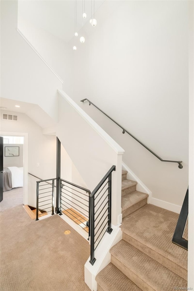 stairs with a towering ceiling, baseboards, visible vents, and carpet floors