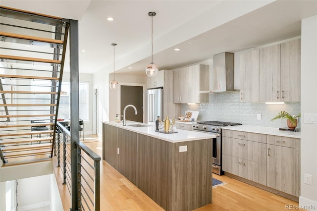 kitchen featuring modern cabinets, light wood-style flooring, a sink, stainless steel appliances, and wall chimney range hood