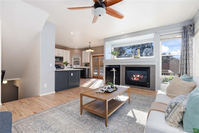 living room with light hardwood / wood-style floors, ceiling fan with notable chandelier, and a fireplace