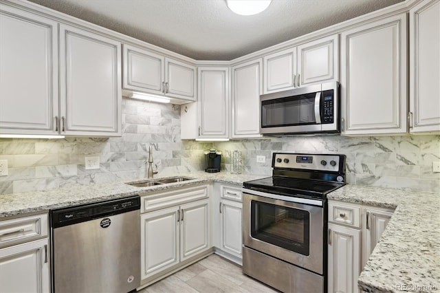 kitchen with tasteful backsplash, white cabinets, appliances with stainless steel finishes, light stone countertops, and a sink