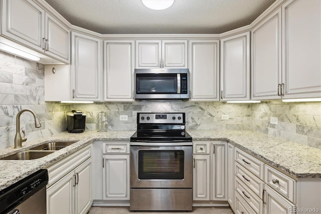 kitchen featuring appliances with stainless steel finishes, a sink, light stone countertops, and tasteful backsplash