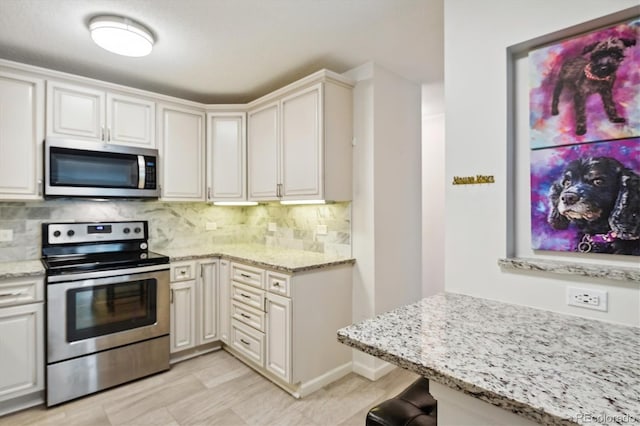 kitchen featuring stainless steel appliances, white cabinets, decorative backsplash, and light stone countertops