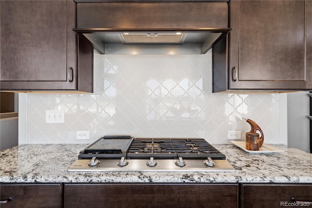 kitchen with light stone counters, backsplash, stainless steel gas cooktop, and wall chimney exhaust hood