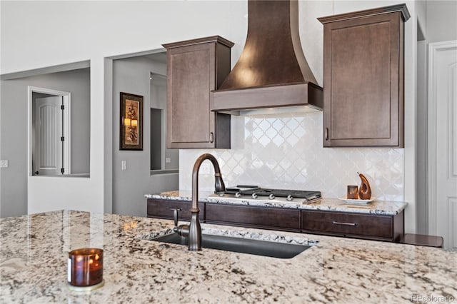 kitchen with light stone counters, sink, custom range hood, and backsplash