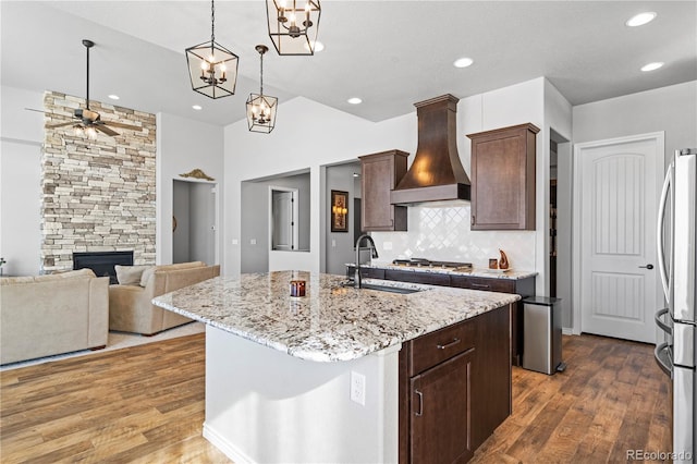 kitchen with sink, light stone counters, a fireplace, custom range hood, and a center island with sink