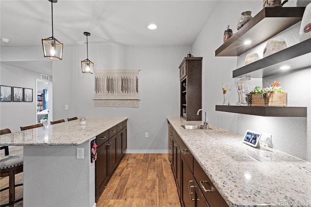 kitchen featuring light stone counters, a kitchen bar, decorative light fixtures, and light wood-type flooring