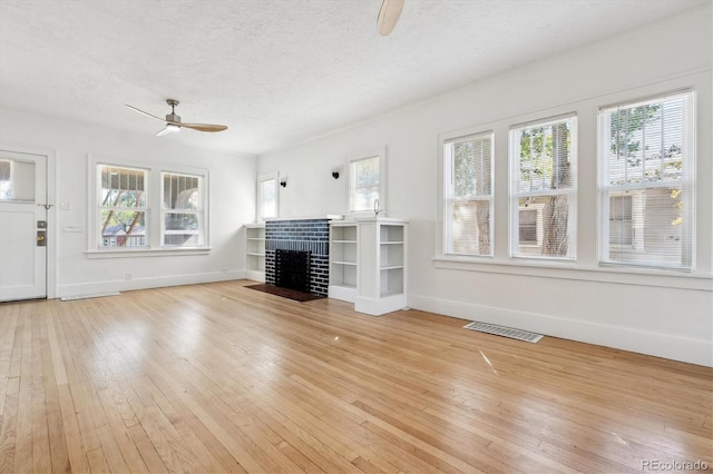 unfurnished living room with ceiling fan, light hardwood / wood-style floors, a fireplace, and a textured ceiling