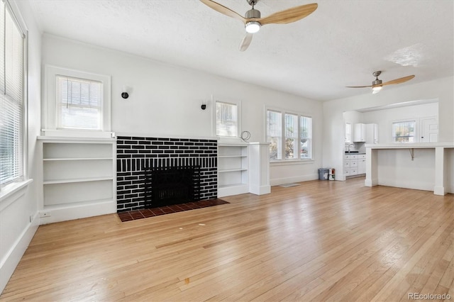 unfurnished living room with a brick fireplace, ceiling fan, light hardwood / wood-style floors, and a wealth of natural light