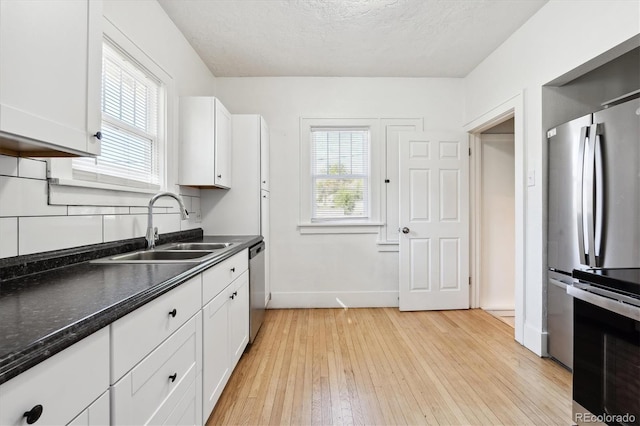 kitchen with appliances with stainless steel finishes, light hardwood / wood-style floors, white cabinetry, and a wealth of natural light