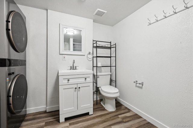 bathroom with stacked washer / dryer, hardwood / wood-style floors, vanity, and toilet