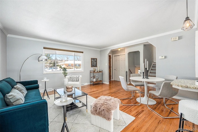 living area featuring arched walkways, baseboards, light wood-style floors, ornamental molding, and stairway