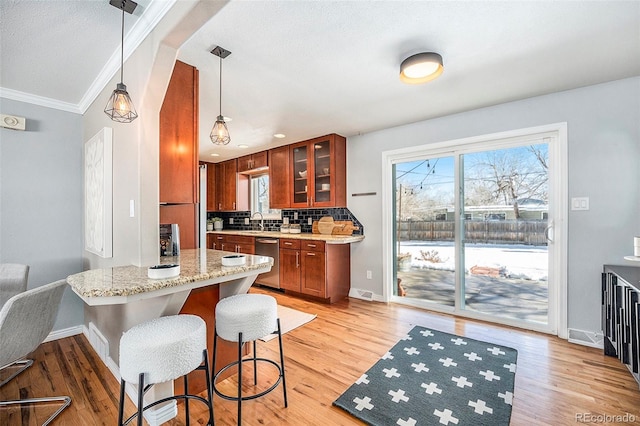 kitchen featuring light stone counters, hanging light fixtures, stainless steel dishwasher, decorative backsplash, and glass insert cabinets