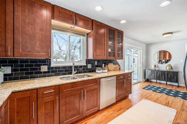 kitchen with stainless steel dishwasher, a sink, glass insert cabinets, and light stone countertops