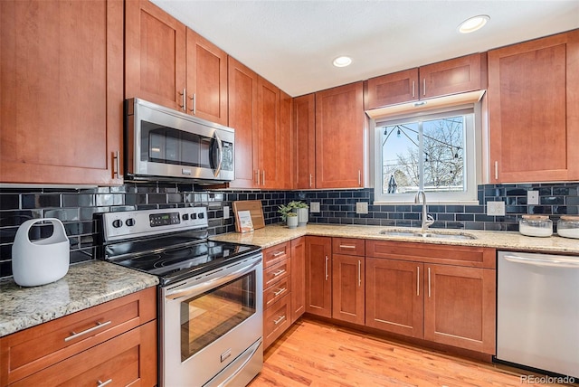 kitchen featuring light stone counters, brown cabinets, appliances with stainless steel finishes, light wood-style floors, and a sink